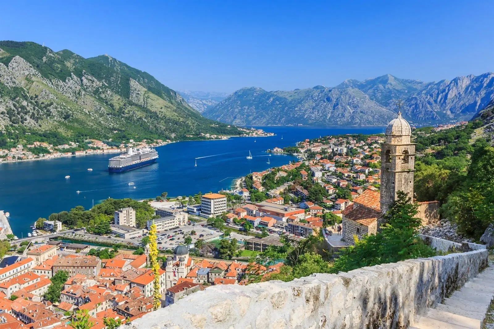 Panoramic view over the Bay of Kotor from the fortress walls, with red-roofed old town, a cruise ship, and steep limestone mountains